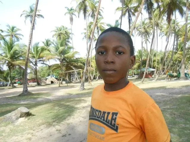 Okeoghene in an orange T-shirt under palm trees